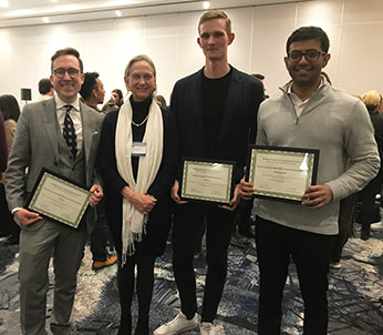 A group of four people in a line in a room holding certificates in front of them