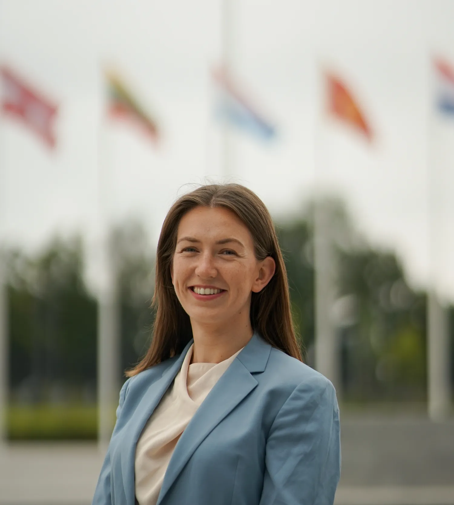 Image of a woman in front of some flags smiling at the camera