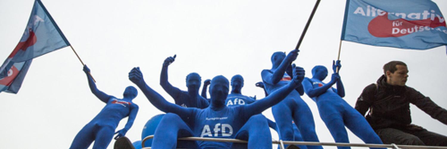 Protestors in blue sitting on top of a bus waving flags. 