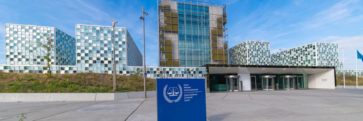 Entrance and main gate of the International Criminal Court building in the Hague under a sunny and blue autumn sky behind a dune with small leafless trees