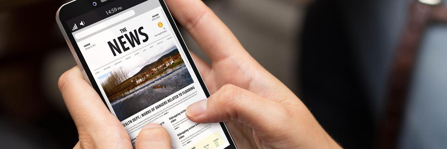 A pair of hands holding a mobile phone showing a news page on it