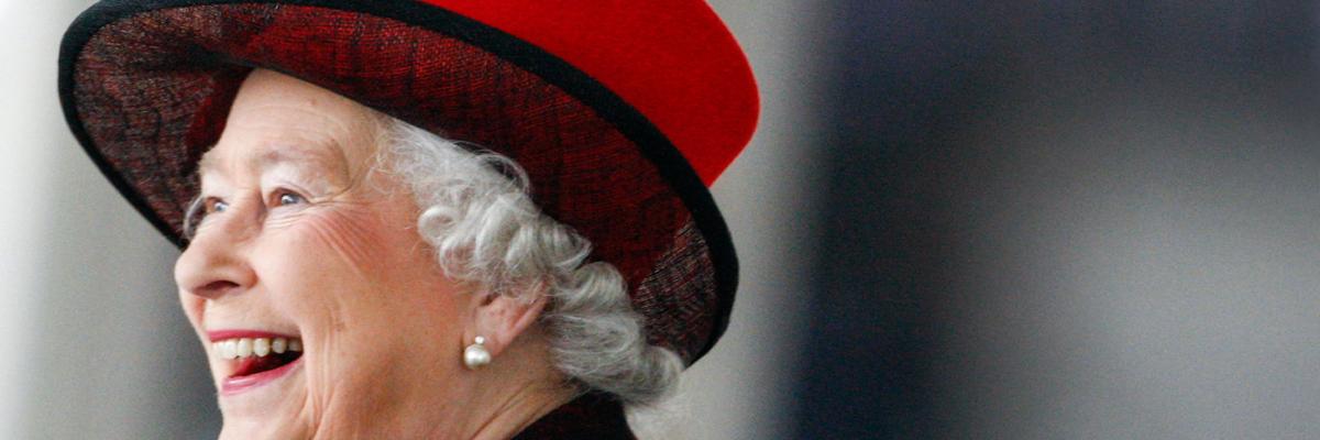 Side view image of Her Royal Highness Queen Elizabeth II smiling and wearing a red hat and a dark top