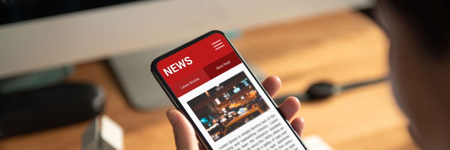 Image of a woman looking at a mobile phone screen with news on sat at a desk