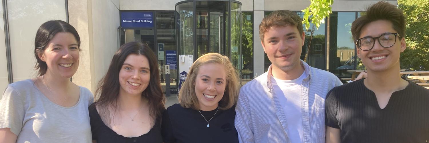 five people stand smiling in front of the Department buidling