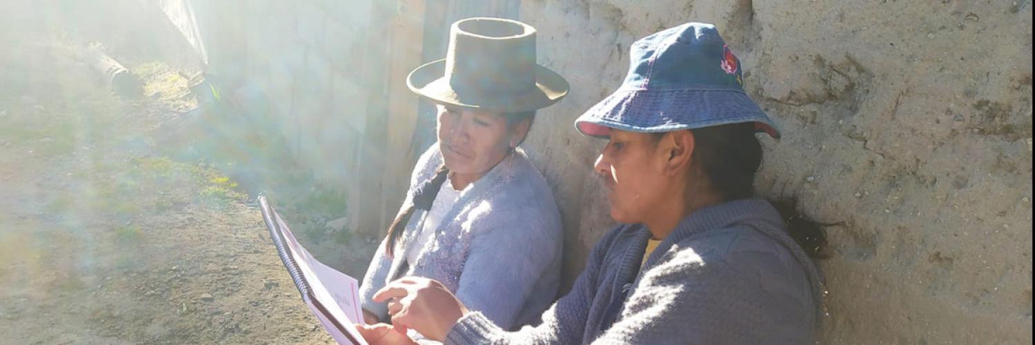 Image of a man and a woman sat against a wall in the sunshine, one holding a document