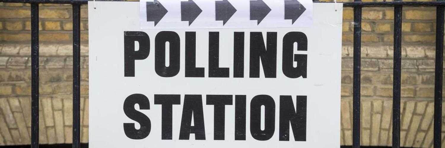 image of a sign saying "polling station' tied to a fence