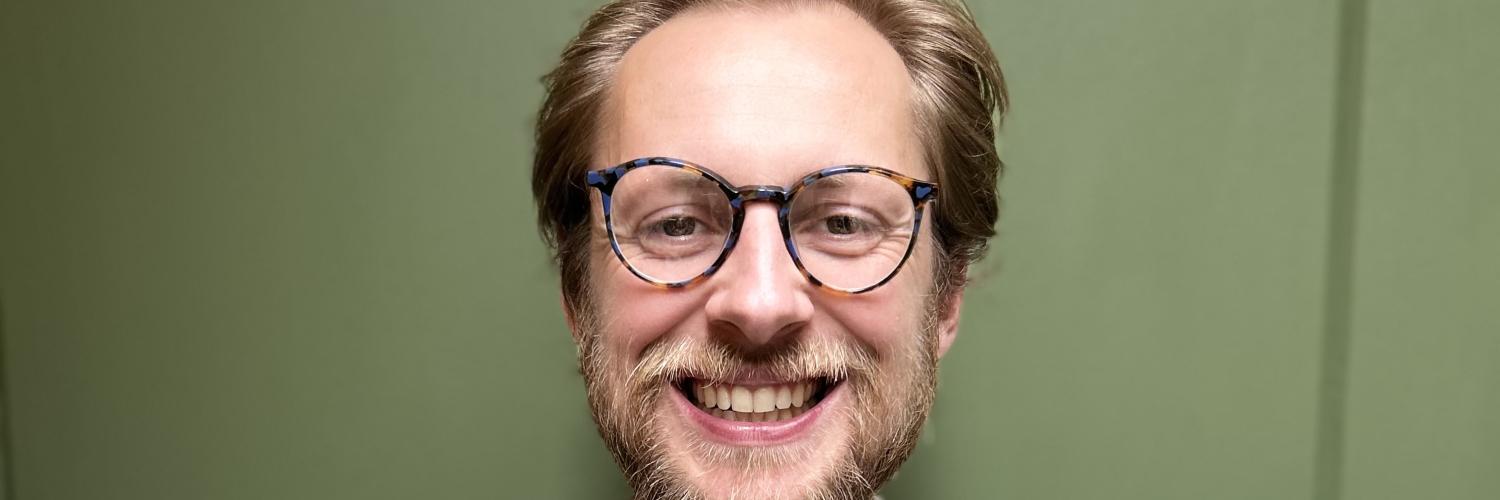 a person wearing glasses in a shirt smiling at the camera