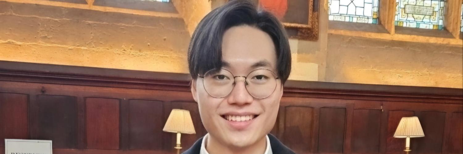 Image of a man wearing glasses and a dark blazer smiling at camera