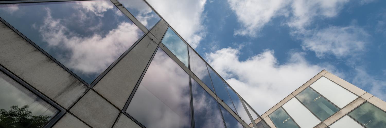 Upwards image of the glasswork of a building set against a cloudy sky. Image