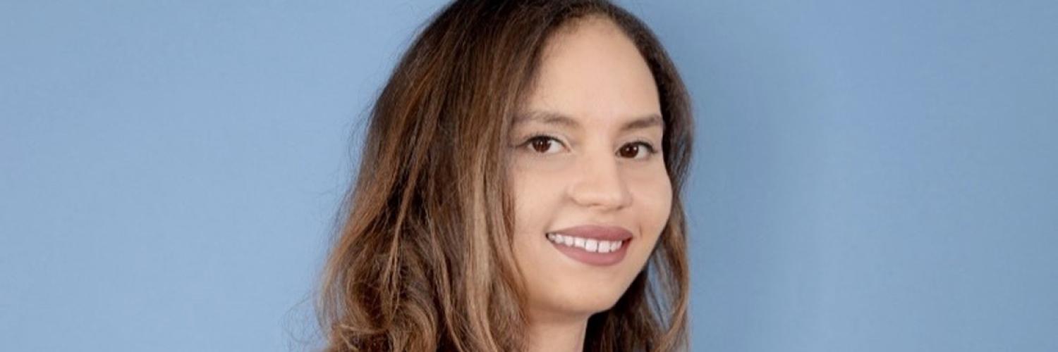 side image of a woman with long hair against a light blue background smiling at the camera