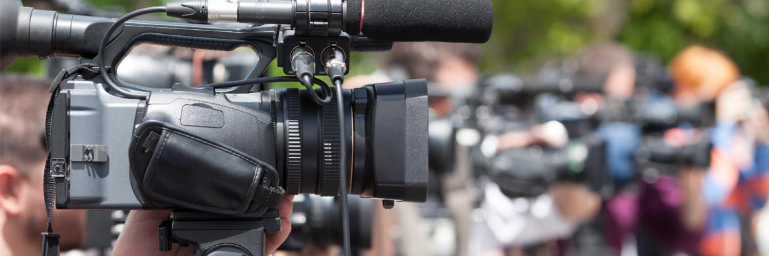 side view of a man holding a video camera with a crowd in the background