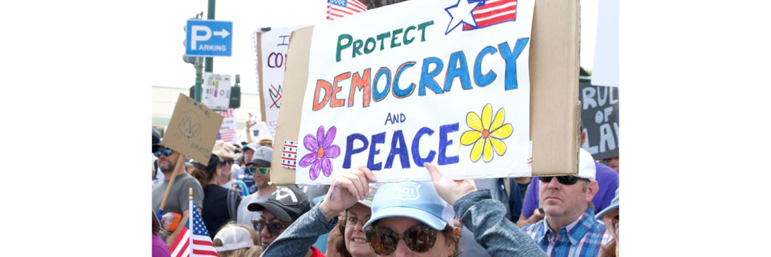 image of a group of people protesting holding a sign reading 'Protect democracy and peace'