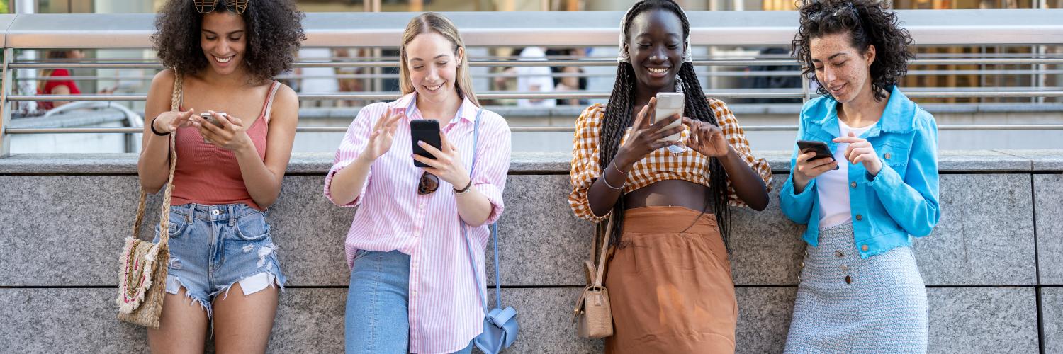 image of four girls stood against a wall looking at their smartphones