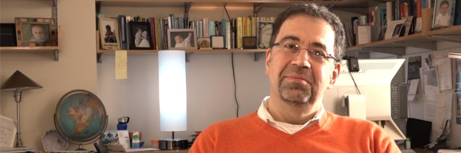 Image of a man in an orange jumper wearing glasses smiling at the camera