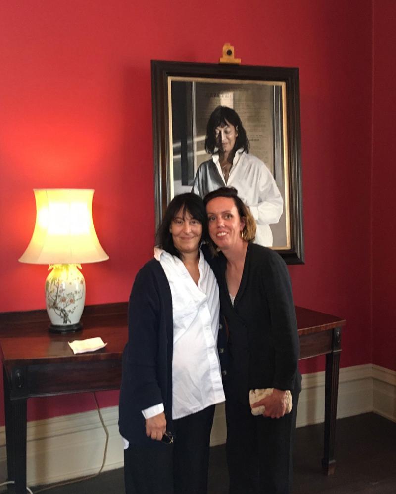 A couple of women posing for a picture in front of a painting