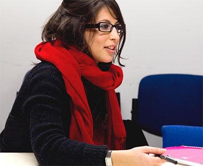 An image of a woman wearing glasses sat sideways working at a desk
