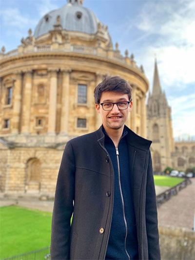 Image of a man wearing glasses smiling at camera in front of a building