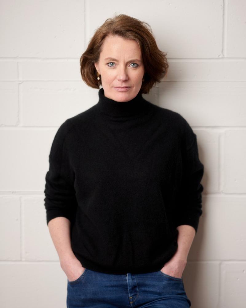 a woman wearing a dark top and blue jeans smiling at camera.