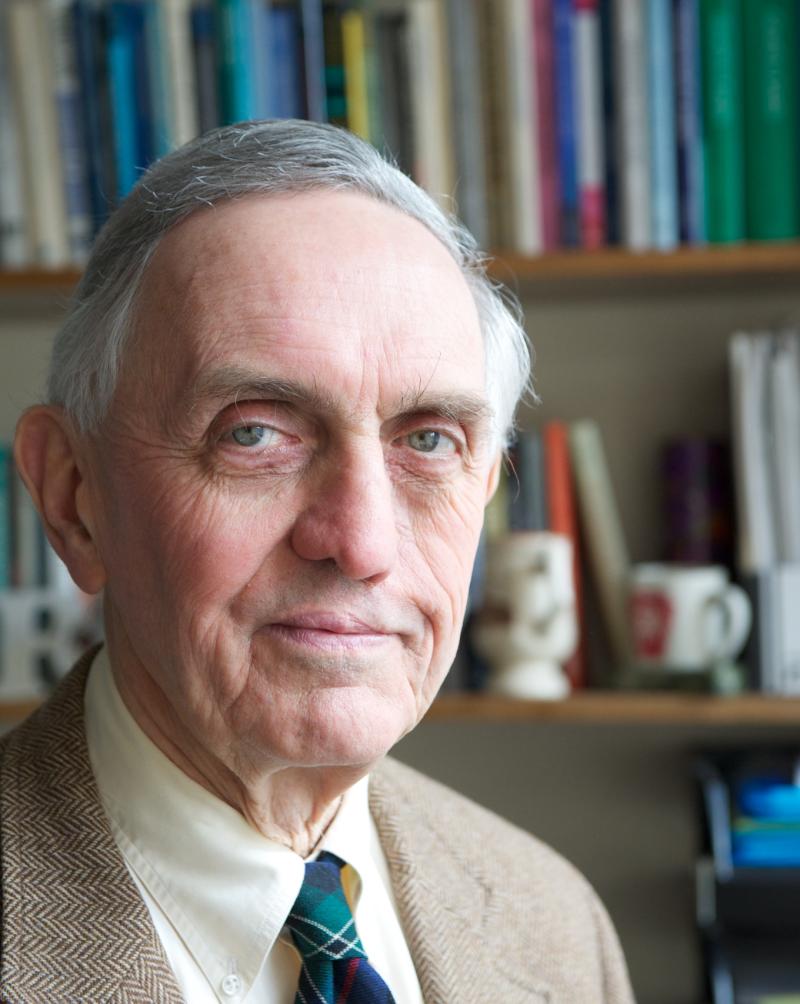 Image of a man in front of a book shelf with a suit and tie smiling at the camera