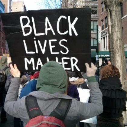 A crowd of people, with some holding placards - one being a 'black lives matter' placard