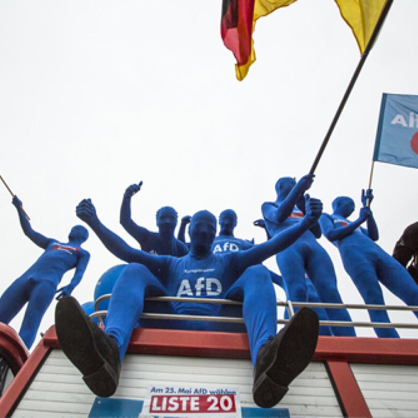 Protestors in blue sitting on top of a bus waving flags. 