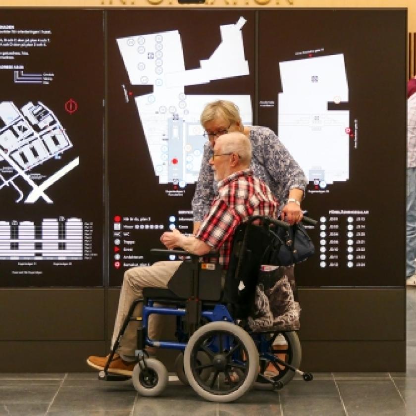 Image of a man in a wheelchair in front of a sign inside a building.