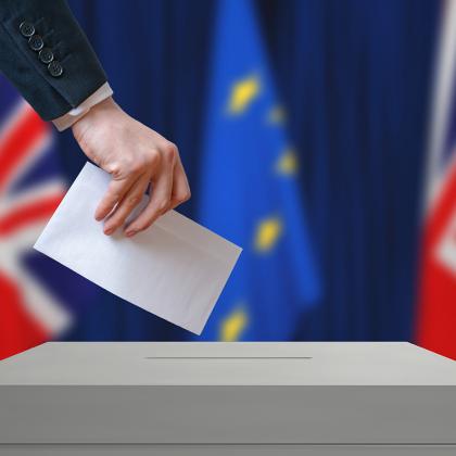 Someone posting a ballot paper in a ballot box, with the Union Jack and E.U flags in the background
