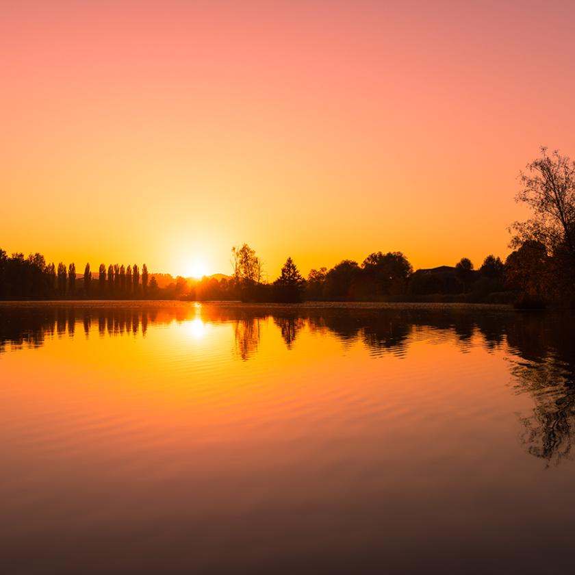 A scenic view of the sun reflecting on a calm sea during a beautiful sunset