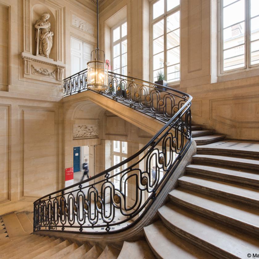 Indoors, person walking at the bottom of a grand staircase