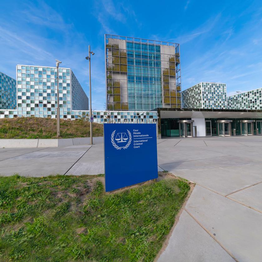 Entrance and main gate of the International Criminal Court building in the Hague under a sunny and blue autumn sky behind a dune with small leafless trees