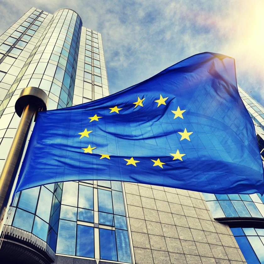 EU flag in front of a tower block with the sun in the sky