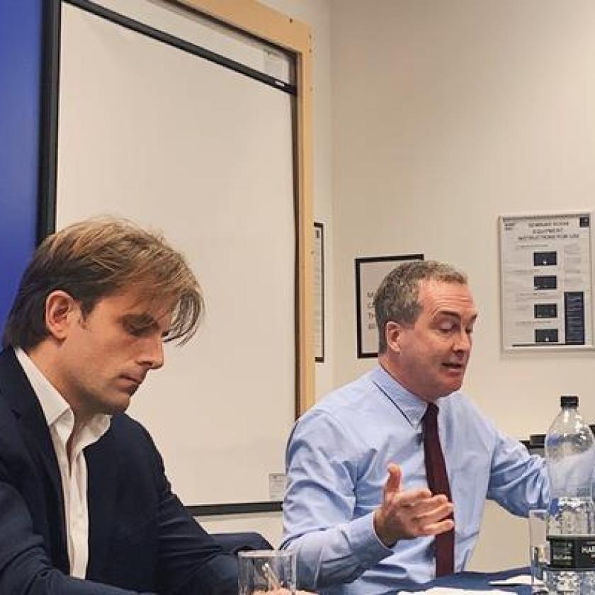 Two men sat at a table presenting in front of an audience