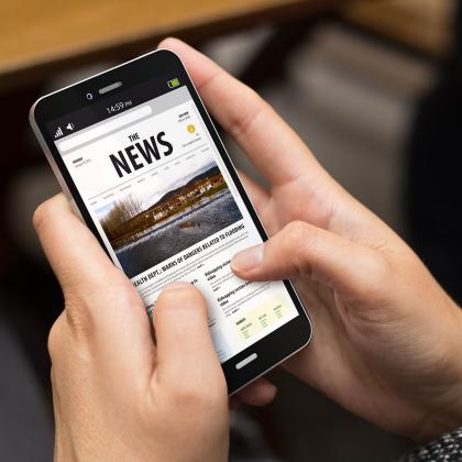 A pair of hands holding a mobile phone showing a news page on it