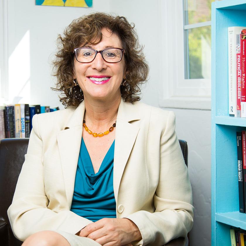 Image of a lady looking at camera with a bookshelf to the right of her and books behind her