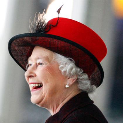 Side view image of Her Royal Highness Queen Elizabeth II smiling and wearing a red hat and a dark top
