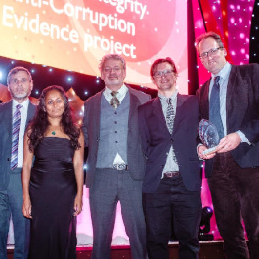 A group of five people on a stage smiling at camera and holding an award