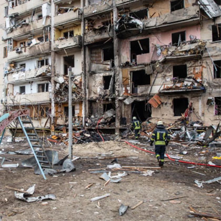 Image of a damaged building with firemen in front of it amidst debris