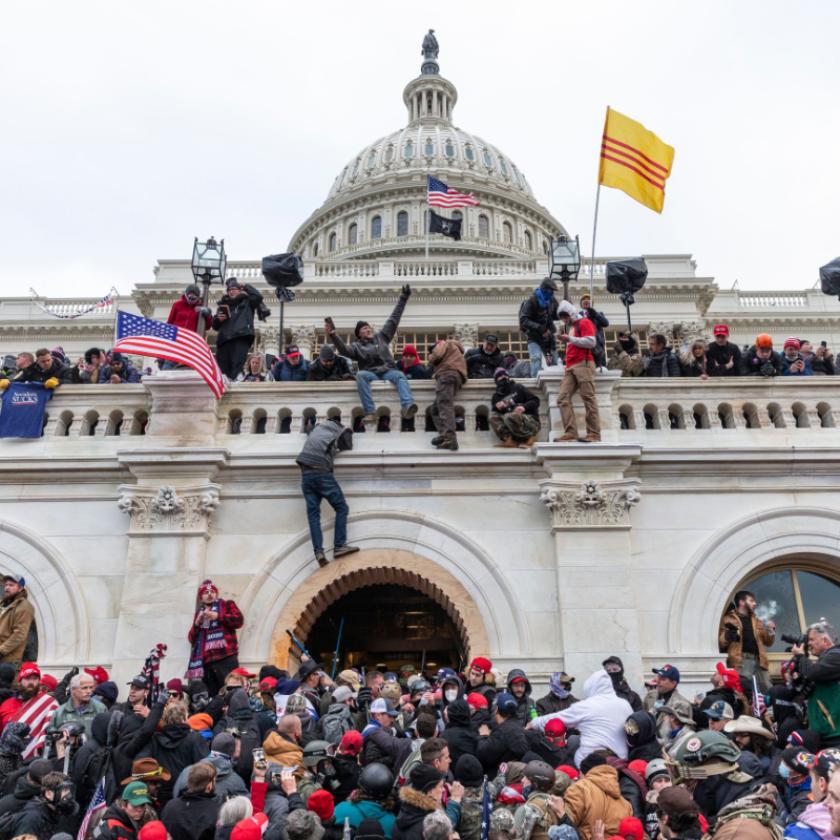 A crowd are climbing a building with various flags