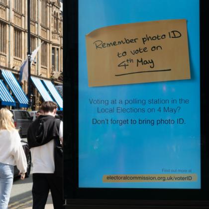 Two people walk past an electronic street sign advertising 'Remember photo ID to vote on 4 May' message from the UK Electoral Commission. 