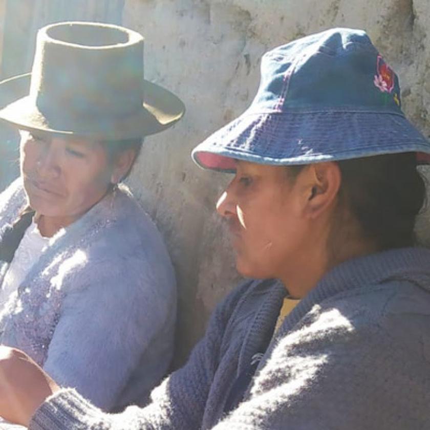 Image of a man and a woman sat against a wall in the sunshine, one holding a document