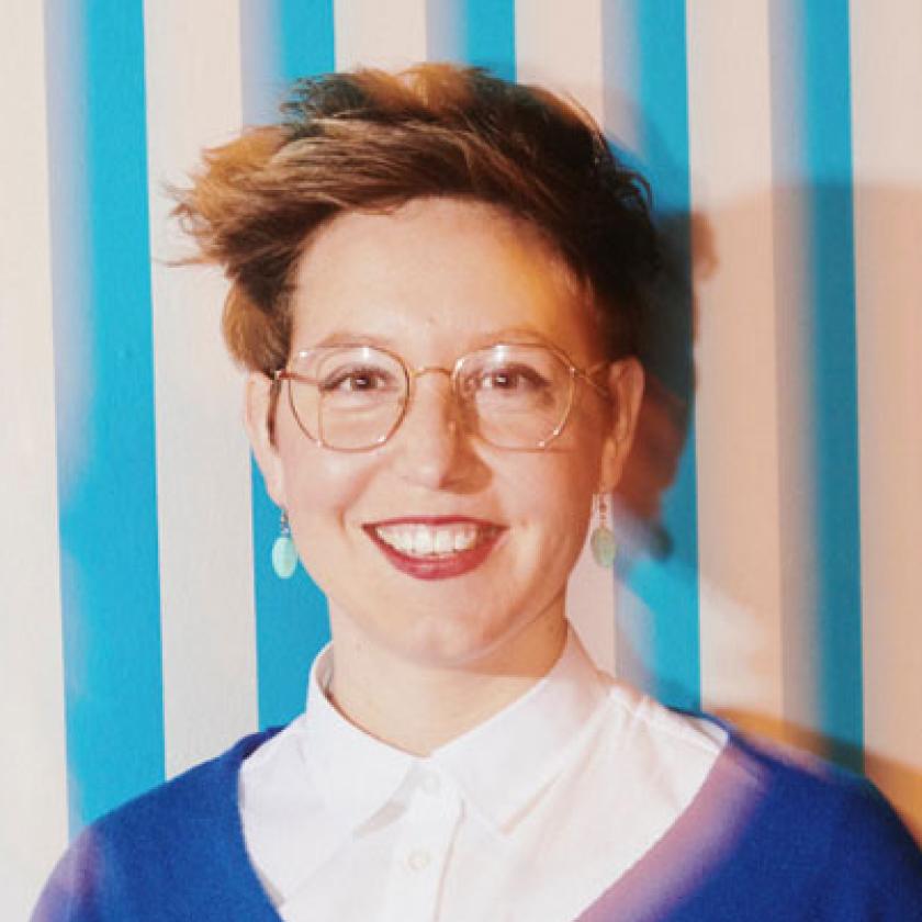 A person smiling in front of a striped wall.