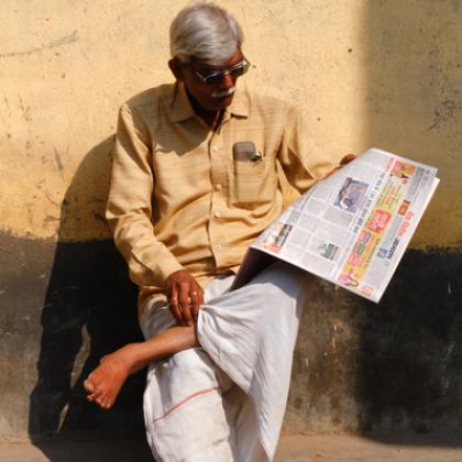 A person sitting on the side of a road reading a newspaper.