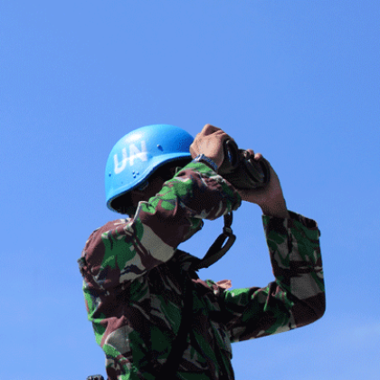A person in camouflage next to a blue flag.