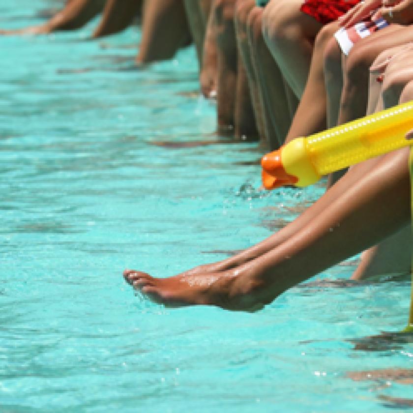 A group of people sitting on the edge of a pool. 