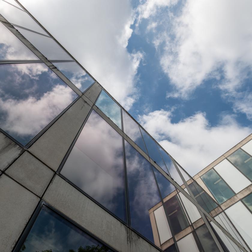 Upwards image of the glasswork of a building set against a cloudy sky. Image