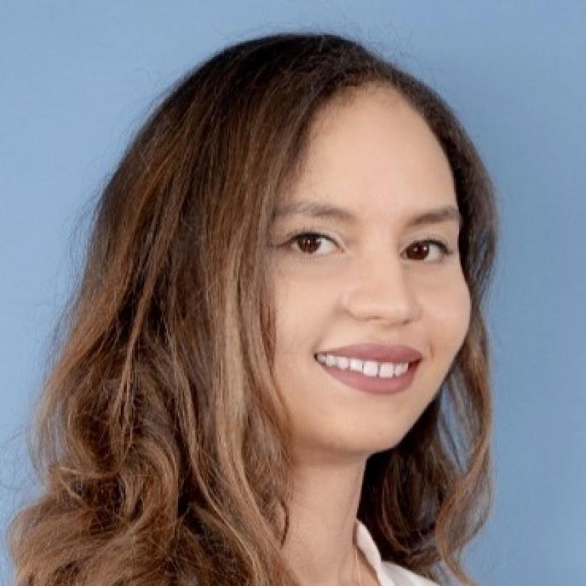side image of a woman with long hair against a light blue background smiling at the camera