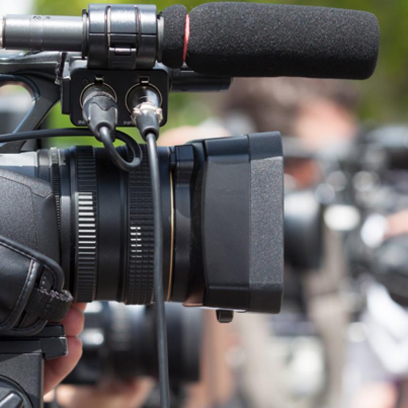 side view of a man holding a video camera with a crowd in the background
