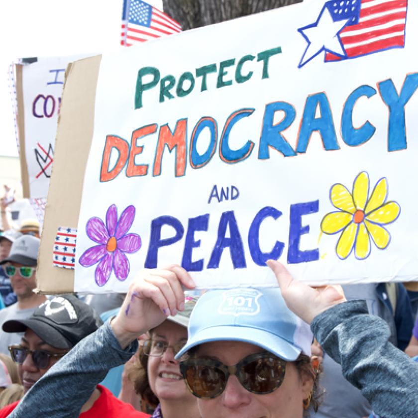image of a group of people protesting holding a sign reading 'Protect democracy and peace'