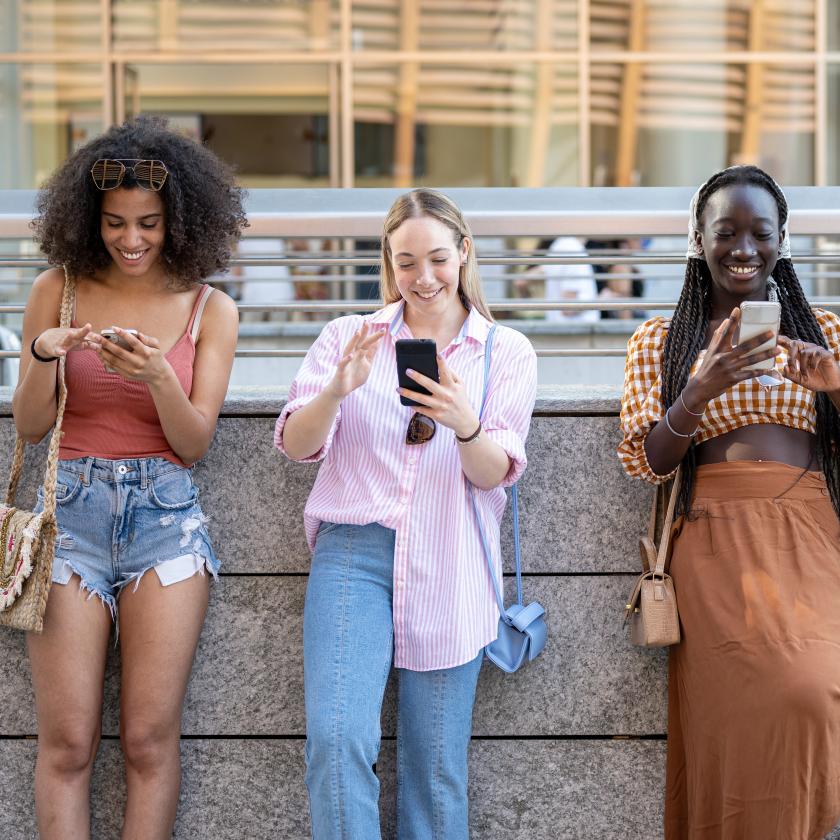 image of four girls stood against a wall looking at their smartphones