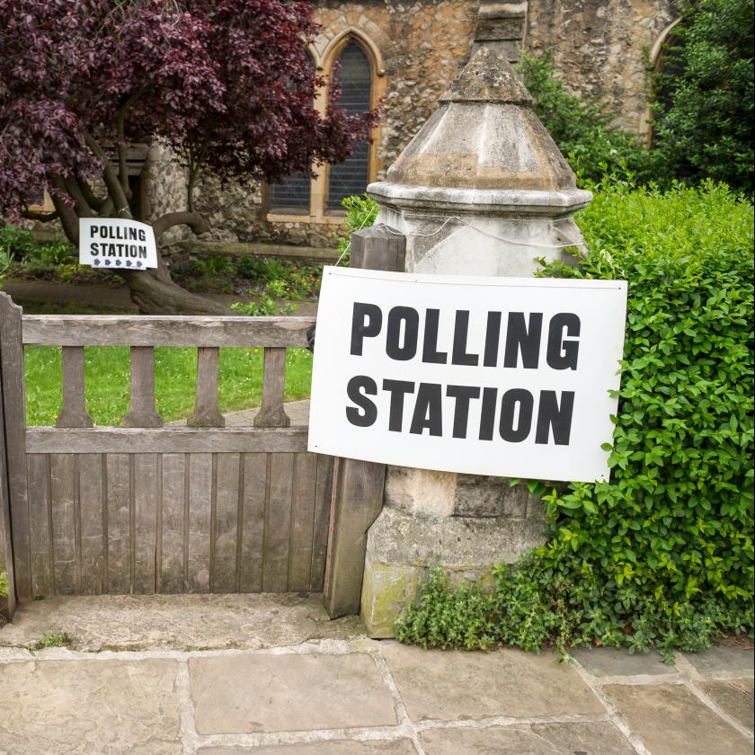 Photograph of an entrance gate to a polling station marked by two white signs with bold black text reading "POLLING STATION." 